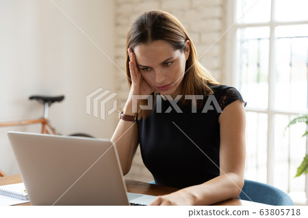 Upset businesswoman sitting at desk reading on laptop unpleasant message 63805718