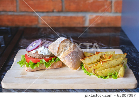 Homemade burger with beef chop, tomato, lettuce and dorblu blue cheese sauce. Serve on a wooden kitchen board on a table made of natural stone. Background image. 63807097