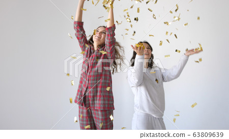 Beautiful happy women dancing through gold glitter confetti on a white background Beautiful happy women dancing through gold glitter confetti on a white background 63809639