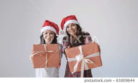Young happy women in Christmas cap gives a gift box on a white background. Holidays packaging, wrapping. Young happy women in Christmas cap gives a gift box on a white background. Holidays packaging, wrapping. 63809644