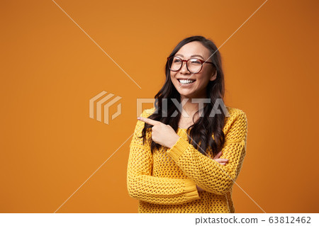 Happy girl in glasses and in jacket points hand to side in studio Happy girl in glasses and in jacket points hand to side in studio 63812462