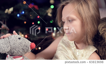 Portrait of a little girl of nine years old in a white festive dress who plays lonely and sadly with a soft toy of a gray rat 63813698