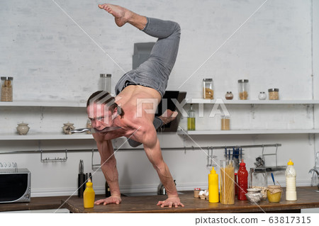 Muscular man keep balance on the hands in the kitchen and holding knife in the mouth. Concept creativity in the kitchen and healthy lifestyle Muscular man keep balance on the hands in the kitchen and holding knife in the mouth. Concept creativity in the kitchen and healthy lifestyle 63817315