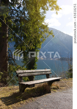 Empty wooden bench on shore of beuatiful lake in austrian Alps. Winter sunny morning on lake Hallstatt. The most beautiful lake to explore in Austria. Empty wooden bench on shore of beuatiful lake in austrian Alps. Winter sunny morning on lake Hallstatt. The most beautiful lake to explore in Austria. 63818251