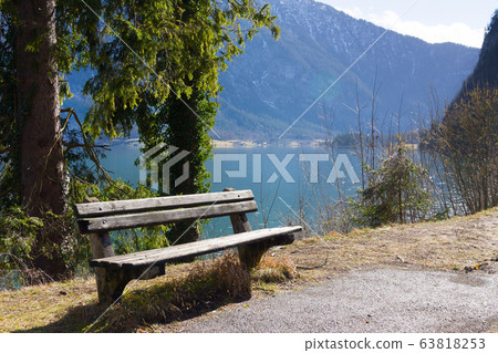 Empty wooden bench on shore of beuatiful lake in austrian Alps. Winter sunny morning on lake Hallstatt. The most beautiful lake to explore in Austria. Empty wooden bench on shore of beuatiful lake in austrian Alps. Winter sunny morning on lake Hallstatt. The most beautiful lake to explore in Austria. 63818253