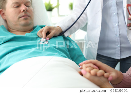Sick man lies on bed in clinic, doctor examines Sick man lies on bed in clinic, doctor examines 63819691