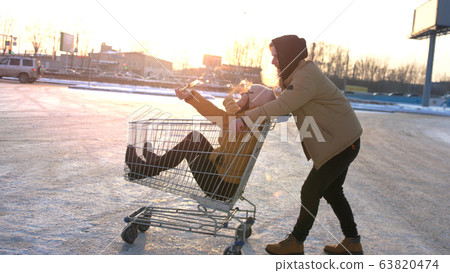 Happy young couple riding on trolley on mall parking. Sun shining on the background. slow motion Happy young couple riding on trolley on mall parking. Sun shining on the background. slow motion 63820474