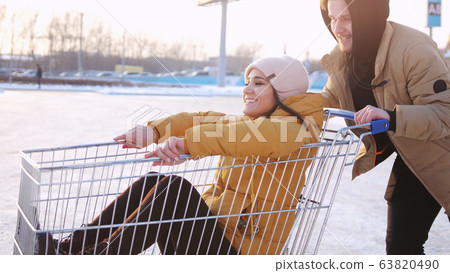 Happy young couple riding on trolley on mall parking. Sun shining on the background. slow motion 63820490