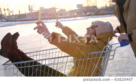 Happy young couple riding on trolley on mall parking. Sun shining on the background. slow motion 63820497