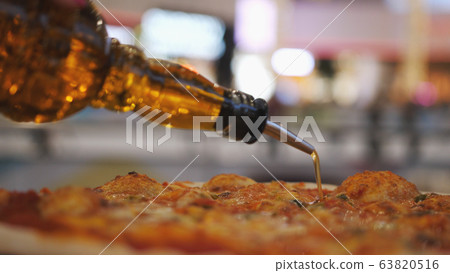 Close-up shot of pouring oil on pizza with blurred lights on background. Close-up shot of pouring oil on pizza with blurred lights on background. 63820516