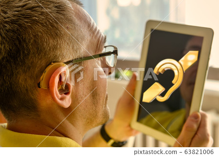 Man wearing deaf aid with tablet 63821006