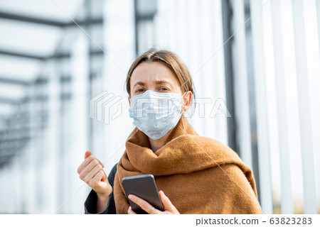 Woman with face mask and smart phone during an epidemic outdoors Woman with face mask and smart phone during an epidemic outdoors 63823283