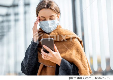 Woman with face mask and smart phone during an epidemic outdoors Woman with face mask and smart phone during an epidemic outdoors 63823289