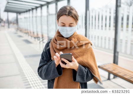 Woman with face mask and smart phone during an epidemic outdoors Woman with face mask and smart phone during an epidemic outdoors 63823291