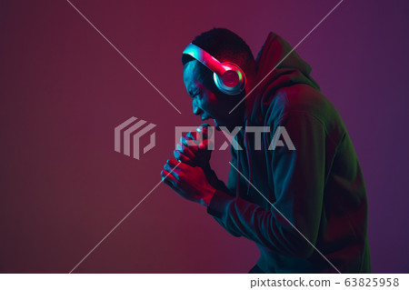 African-american man's portrait with headphones isolated on gradient studio background in neon light 63825958