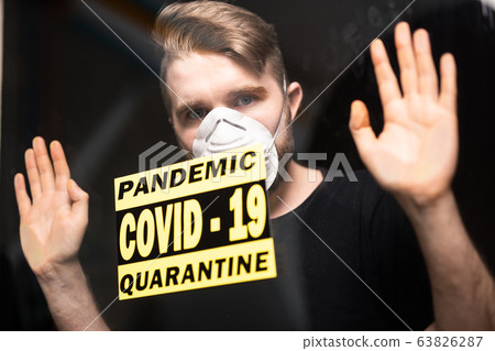 Coronavirus, quarantine, covid-19 and pandemic concept. Sad and sick man of corona virus looking through the window. Stay at home. Coronavirus, quarantine, covid-19 and pandemic concept. Sad and sick man of corona virus looking through the window. Stay at home. 63826287