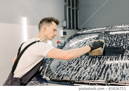 Car wash and clean with shampoo and sponge. Young handsome man worker washing soapy car windshield with sponge on a car wash. Car wash and clean with shampoo and sponge. Young handsome man worker washing soapy car windshield with sponge on a car wash. 63826751