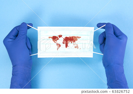 Disposable medical mask with the contour of the continents of the planet in the hands of a doctor on a blue background, pandemic concept. KOVID-19, coronavirus. The global epidemic of the disease. 63826752