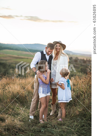Happy smiling young family, father, mother and two little daughters having fun outdoors, standing together in a wild field. Mom and Dad talking with their kids, laughing, enjoying time together Happy smiling young family, father, mother and two little daughters having fun outdoors, standing together in a wild field. Mom and Dad talking with their kids, laughing, enjoying time together 63826895