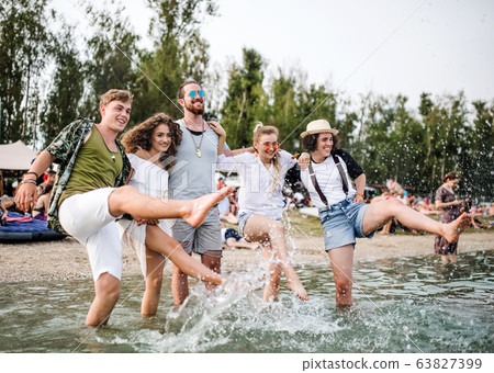 Group of young friends at summer festival, standing in lake. 63827399