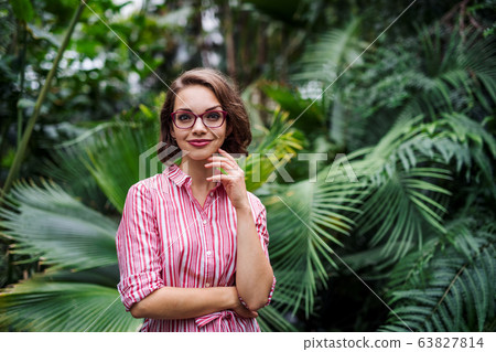 Young woman standing in botanical garden, looking at camera. Young woman standing in botanical garden, looking at camera. 63827814
