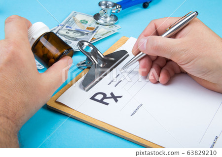Male doctor or pharmacist holding jar or bottle of pills in hand and writing prescription on a special form. medical costs and healthcare payment concept. Male doctor or pharmacist holding jar or bottle of pills in hand and writing prescription on a special form. medical costs and healthcare payment concept. 63829210