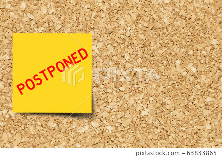 Yellow note with word postoned cork board 63833865