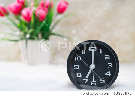 Black alarm clock and flower in vase on table Black alarm clock and flower in vase on table 63833976