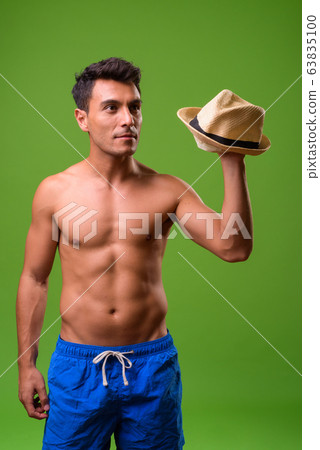 Young handsome Hispanic man shirtless against green background 63835100