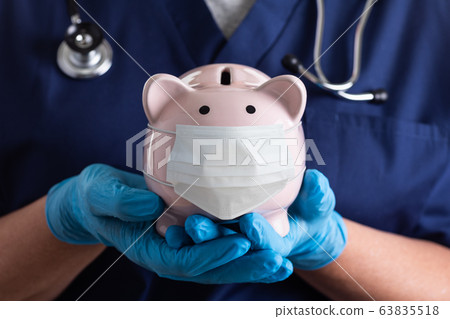 Doctor or Nurse Wearing Surgical Gloves Holding Piggybank 63835518