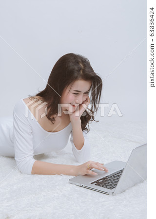 Young Asian woman using the laptop computer and lying on white bed at home. Young Asian woman using the laptop computer and lying on white bed at home. 63836424