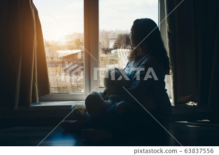 Woman with Teddy bear by the window. Girl looking out. Concept oflife style, toys, holidays Woman with Teddy bear by the window. Girl looking out. Concept oflife style, toys, holidays 63837556