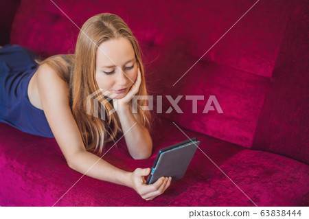 Young woman reads e-book at home on the couch 63838444