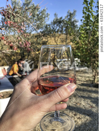 a hand holding a glass of blush wine against a a hand holding a glass of blush wine against a 63842517