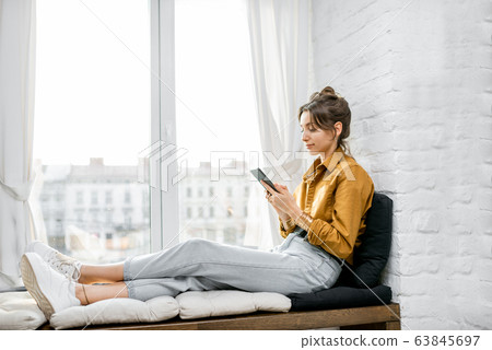 Woman using phone while relax on the window sill at home 63845697