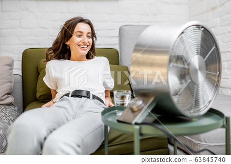 Woman cooling herself with a fan at home 63845740