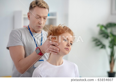 Male physiotherapist holding head of female patient 63854607