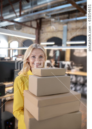 Blonde woman standing with pile of boxes Blonde woman standing with pile of boxes 63854631