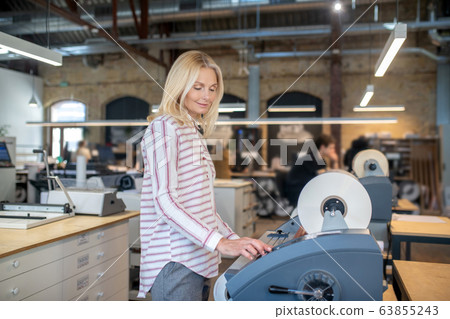 Blonde woman adjusting paper roll machine, smiling 63855243
