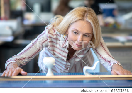 Blonde woman bending, looking at chair maquettes Blonde woman bending, looking at chair maquettes 63855288