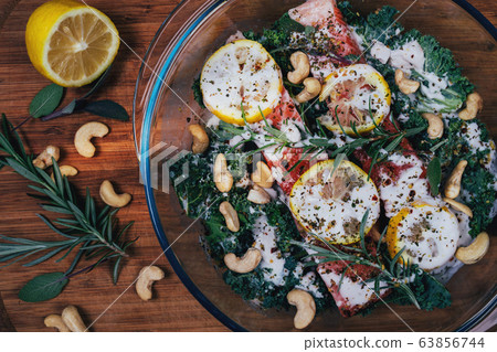 Close up photo of ready to go to oven fish in glass pot with lemon rosemary and cashew nuts Close up photo of ready to go to oven fish in glass pot with lemon rosemary and cashew nuts 63856744