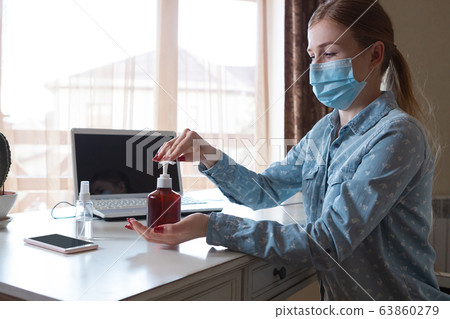 Young woman in face mask disinfecting gadgets surfaces on her workplace 63860279