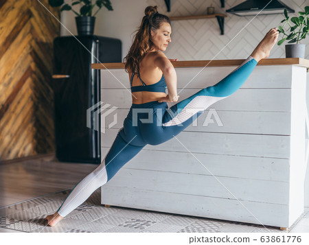 Young woman doing the splits at home with her leg up on the table. Young woman doing the splits at home with her leg up on the table. 63861776