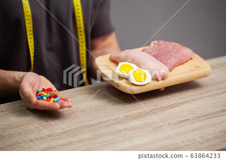 Close up of male hands with food rich in protein on cutting board and pill on table Close up of male hands with food rich in protein on cutting board and pill on table 63864233