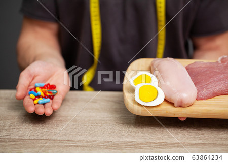 Close up of male hands with food rich in protein on cutting board and pill on table Close up of male hands with food rich in protein on cutting board and pill on table 63864234