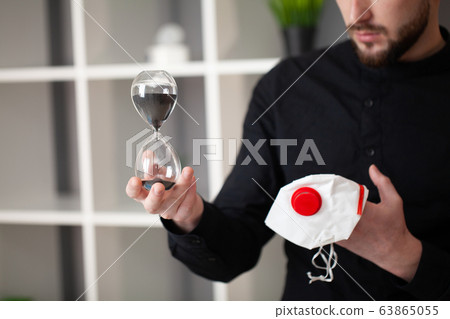Man holds a mask and an hourglass that indicates that time is burning Man holds a mask and an hourglass that indicates that time is burning 63865055