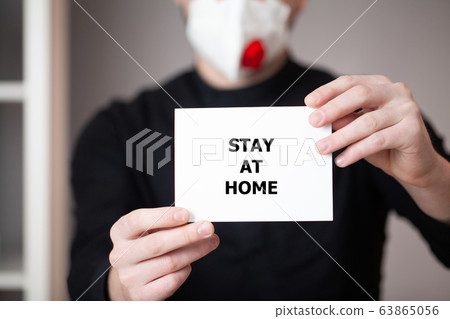 Man in a mask holds a sheet with the inscription stay at home Man in a mask holds a sheet with the inscription stay at home 63865056