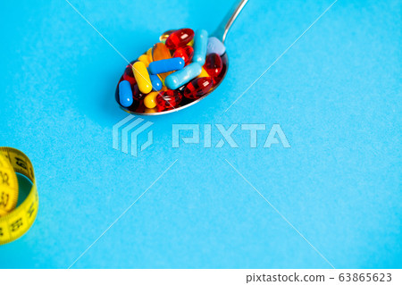 Spoon full of pills for weight loss on blue background Spoon full of pills for weight loss on blue background 63865623