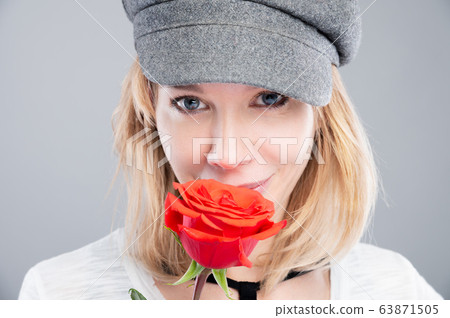 Close-up portrait of an attractive caucasian blonde girl in a retro cap with roses in her hands and looking to the side 63871505