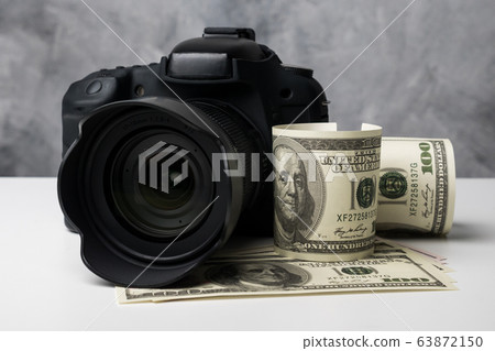 A black digital camera and banknotes on a white table with grunge background. 63872150